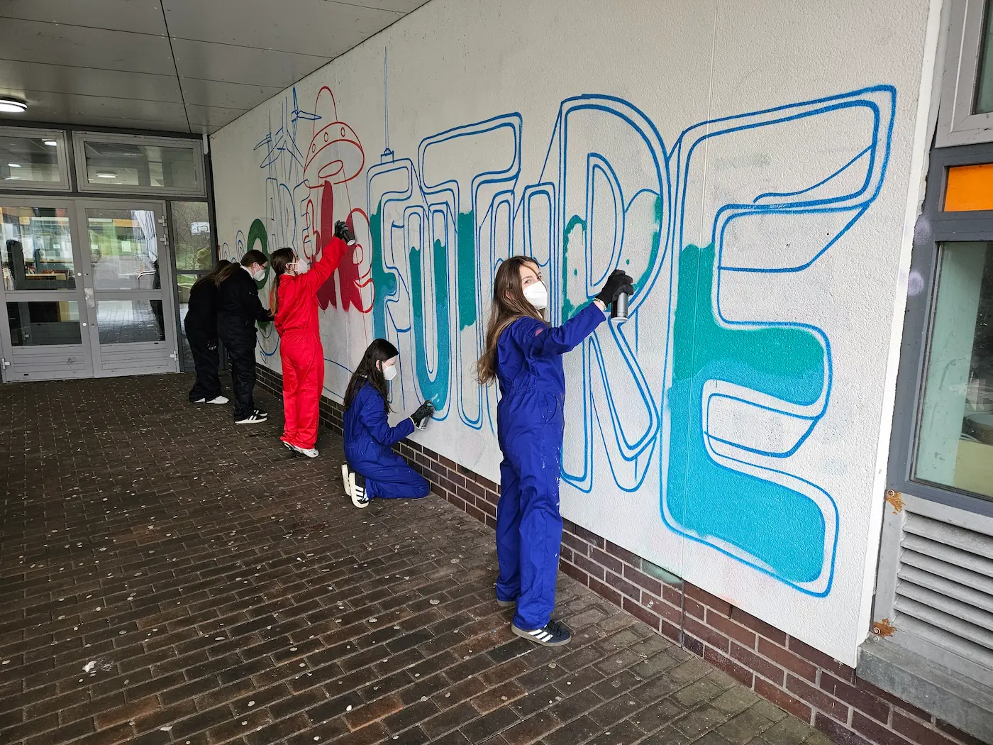 Young people spray-painting a mural under Tragic O'Hara's supervision
